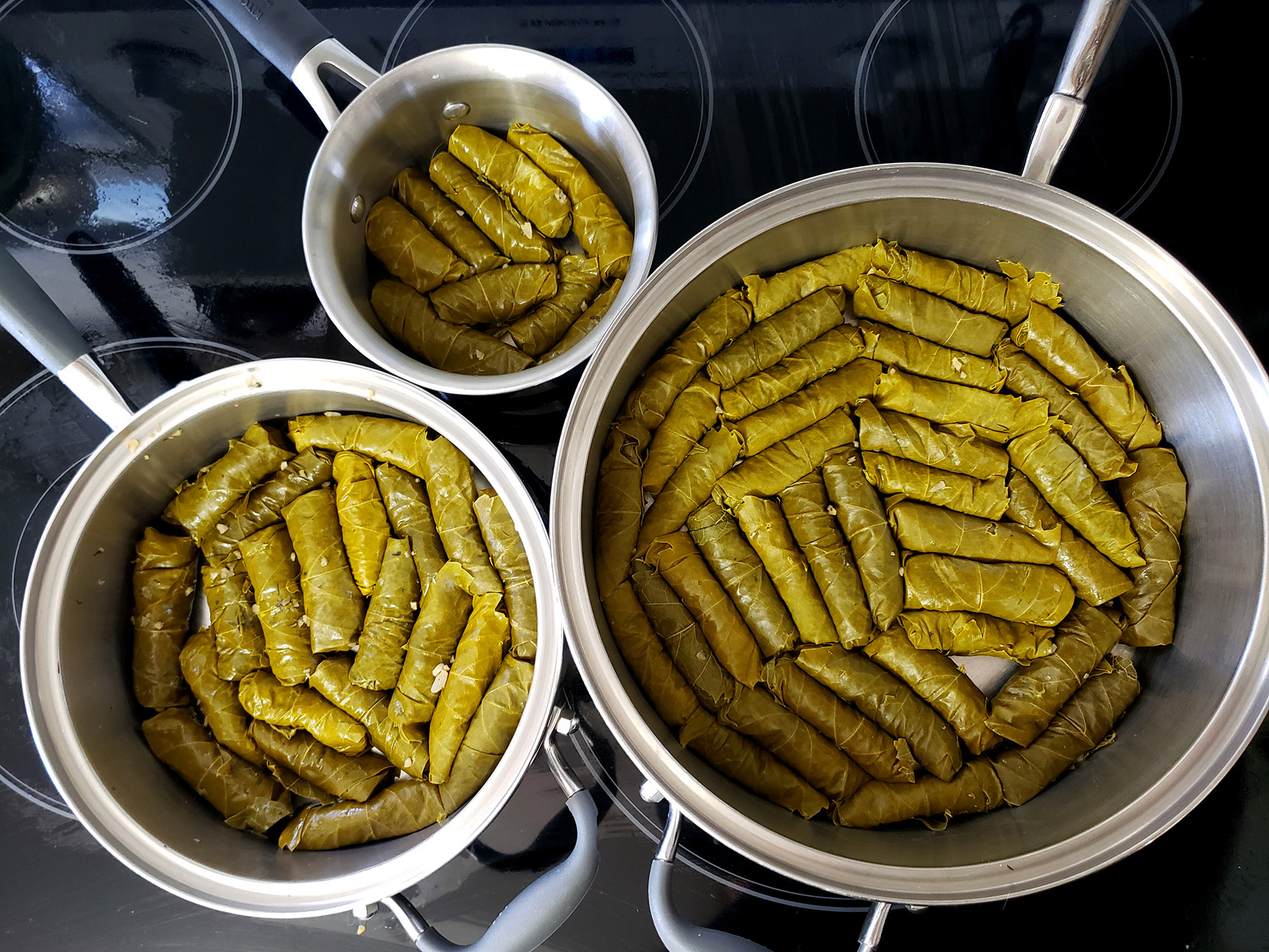 3 pots of various sizes, each with a solid layer of paleo stuffed grape leaves arranged in it.