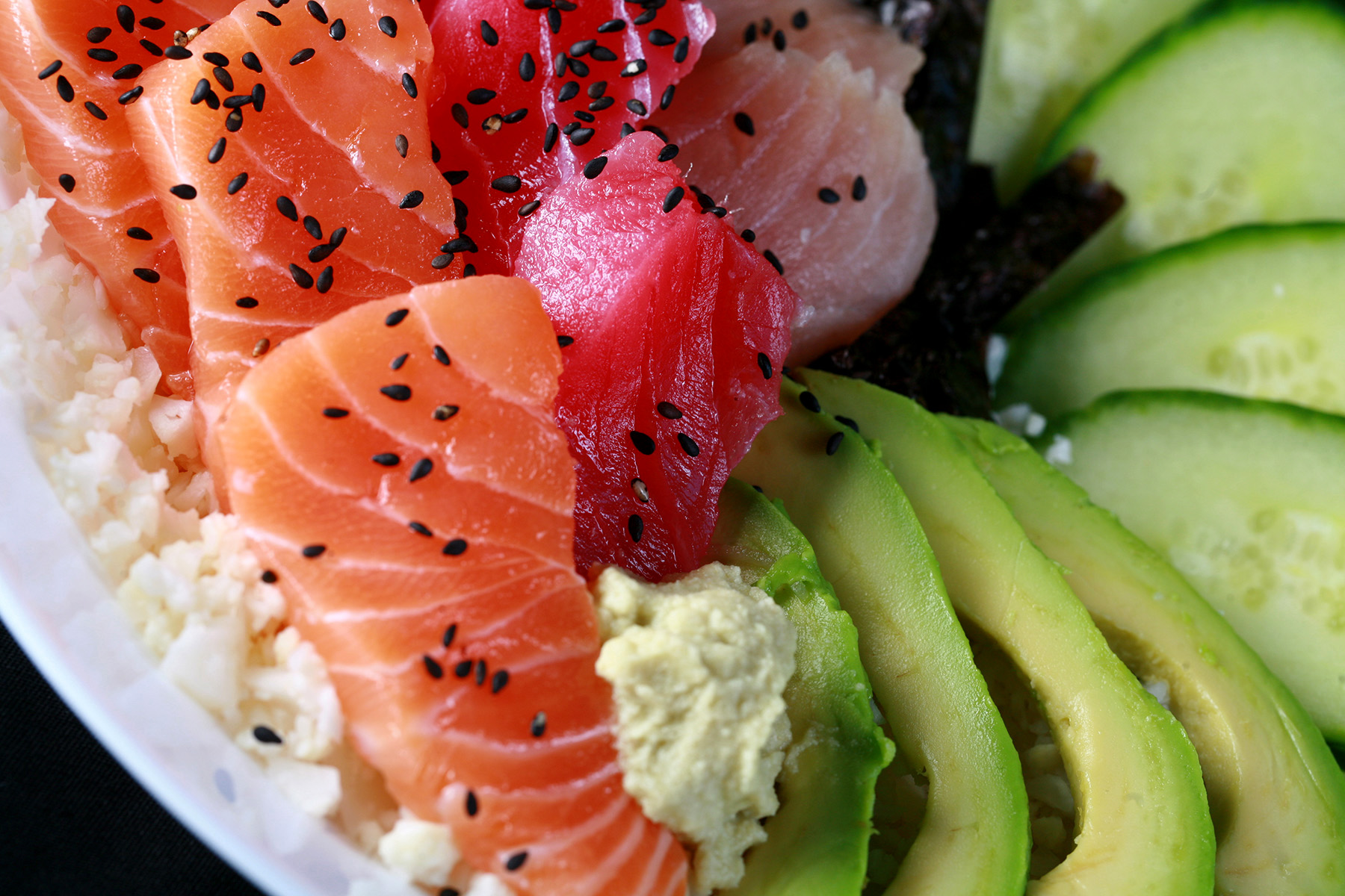 A low carb chirashi bowl - A shallow bowl with various cuts of fish - salmon, tuna, and snapper - as well as some veggies. It is all arranged on top of riced cauliflower.