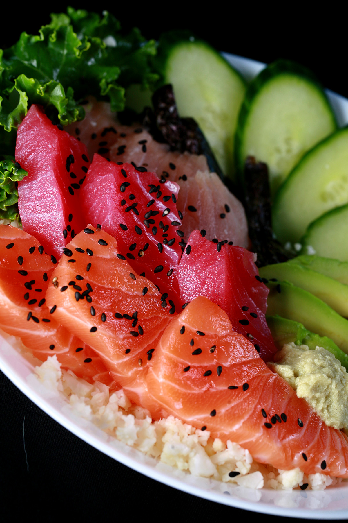 A keto chirashi bowl - A shallow bowl with various cuts of fish - salmon, tuna, and snapper - as well as some veggies. It is all arranged on top of riced cauliflower.