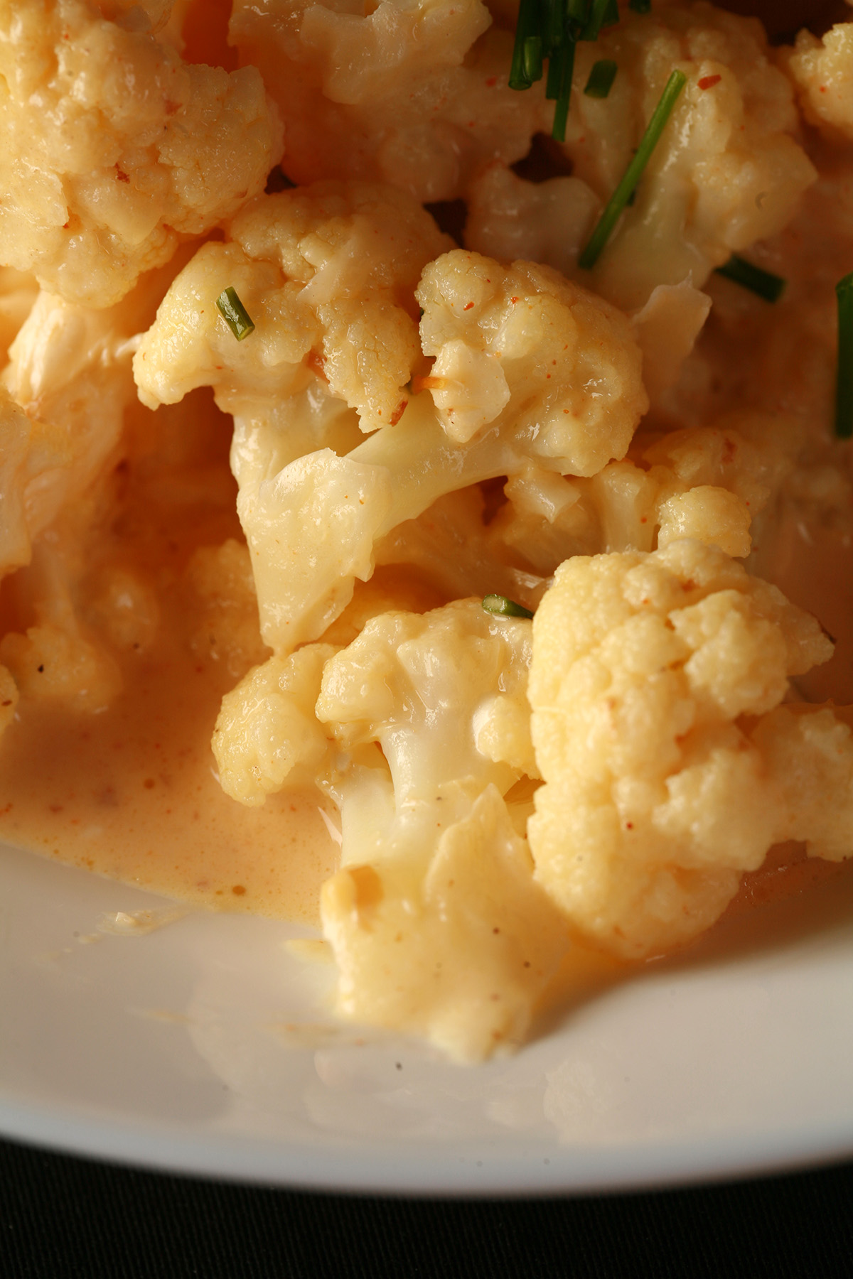 Close up view of a bowl of small pieces of cauliflower, coated in a creamy cheese sauce.