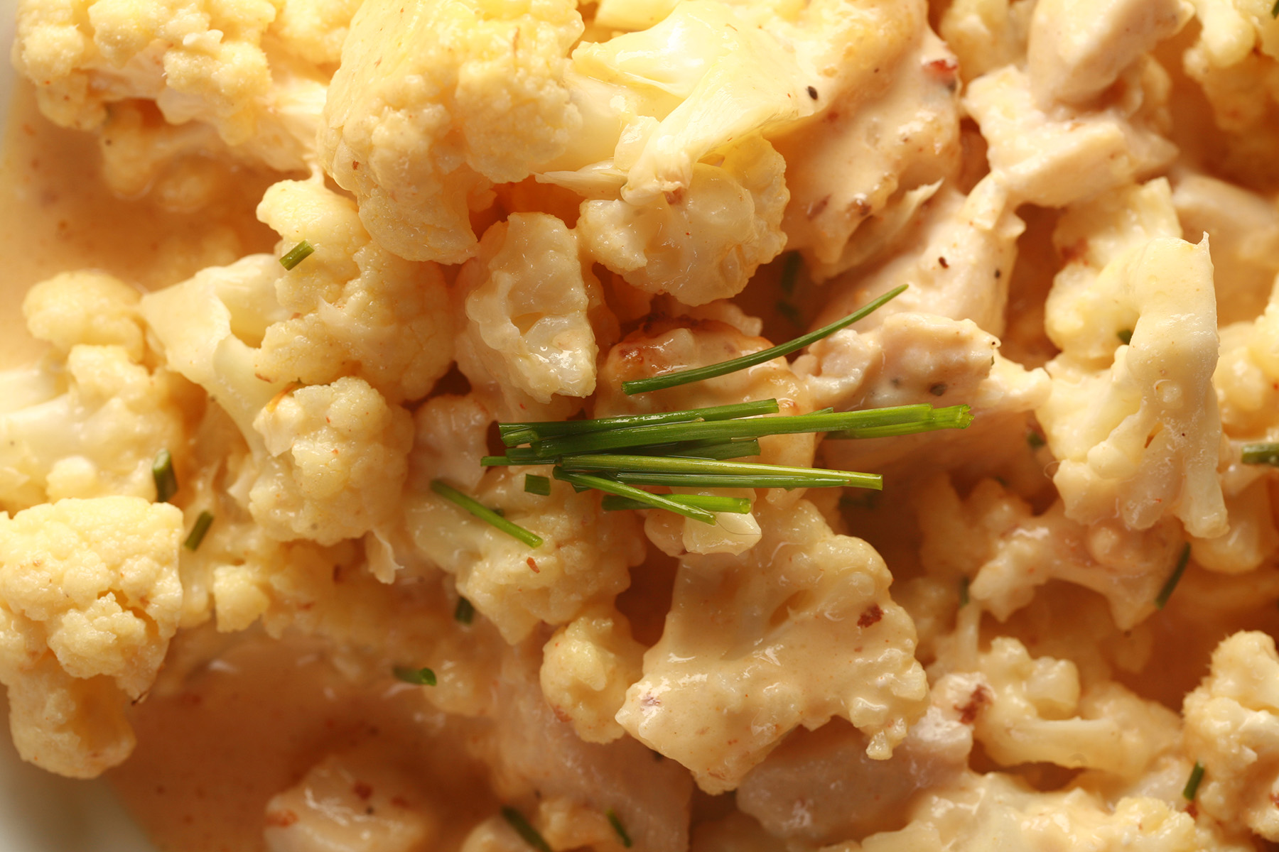 Close up view of a bowl of small pieces of cauliflower, coated in a creamy cheese sauce.