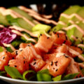 Close up view of a keto spicy salmon poke bowl - chunks of marinated salmon and veggies, drizzled with a light pink dynamite sauce.