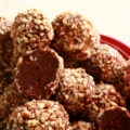 A red plate piled high with low carb bananas foster truffles. They are coated in crushed pecans.