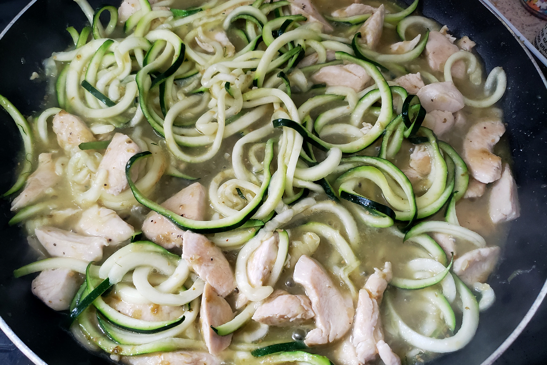 A pan of zuchinni noodles, chicken, and green sauce.