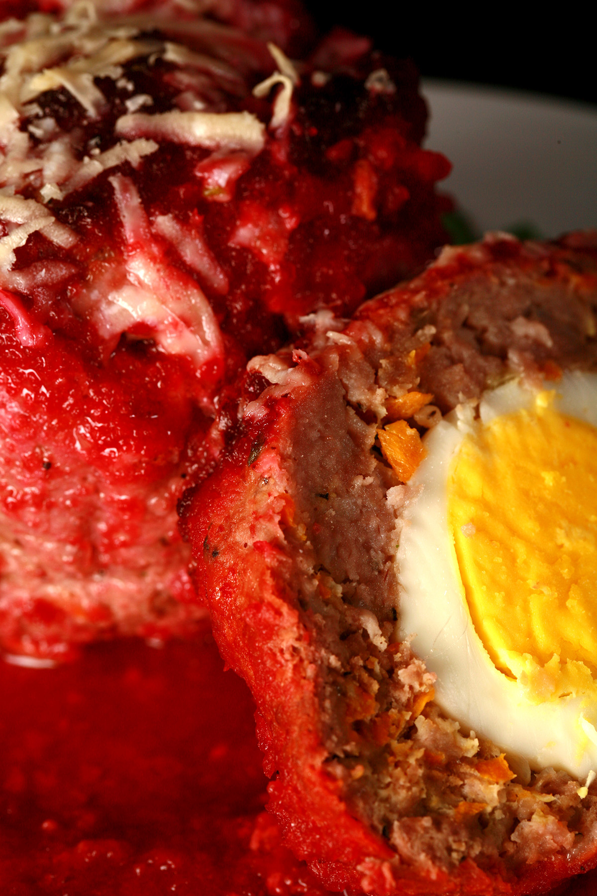 An individual scotch egg meatloaf on a white plate, with a half meatloaf next to it. The half serving shows the hard boiled egg surrounded by meatloaf.
