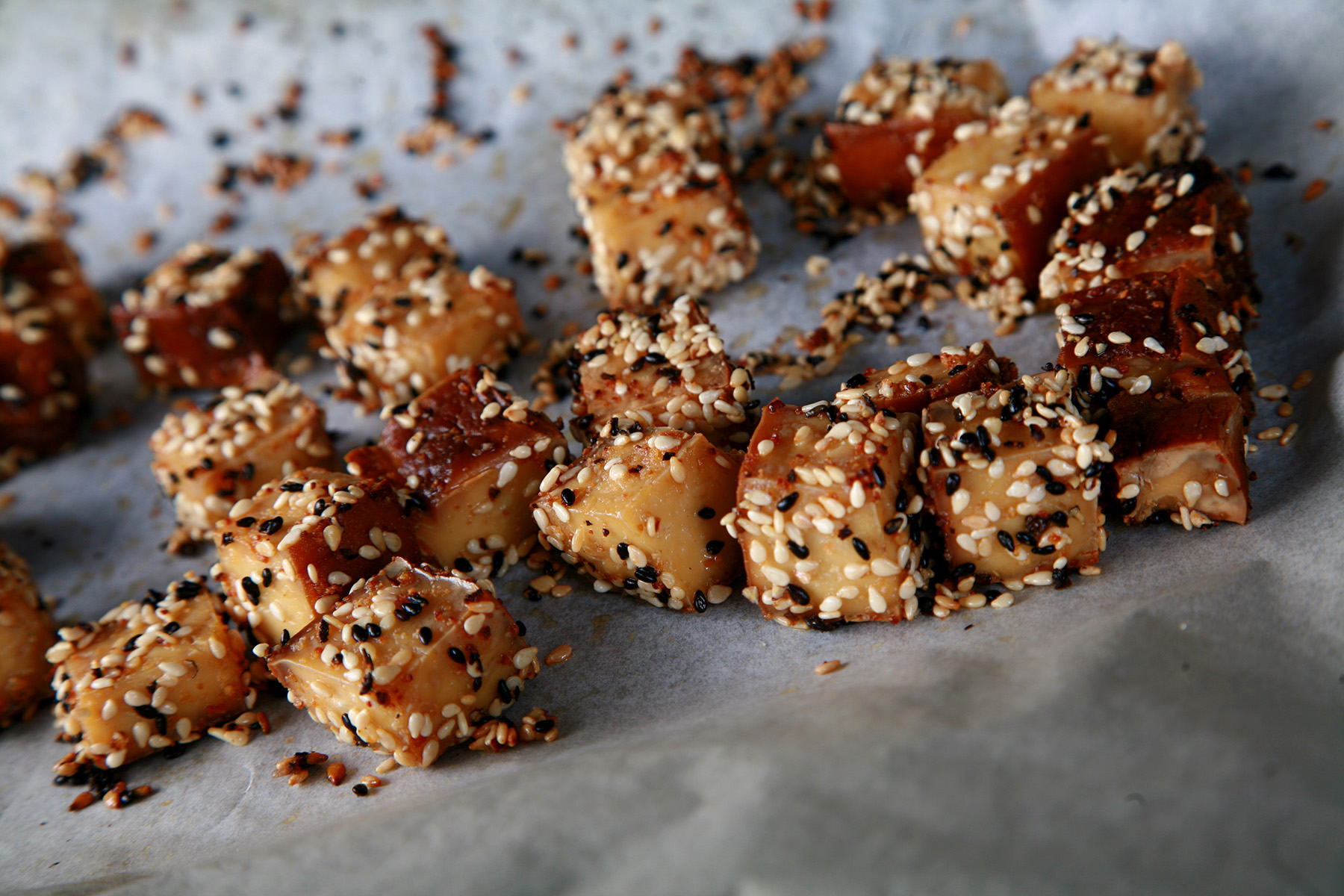 Cubes of smoked tofu on a parchment lined baking sheet. They are coated with sesame seeds.