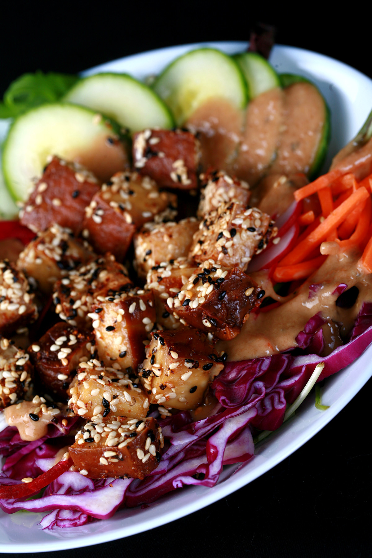 Cubes of sesame crusted smoked tofu on top of a colourful salad. Cucumbers, beets, carrots, and purple cabbage are visible.