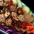 sesame crusted smoked tofu on top of a colourful salad. Cucumbers, beets, carrots, and purple cabbage are visible.