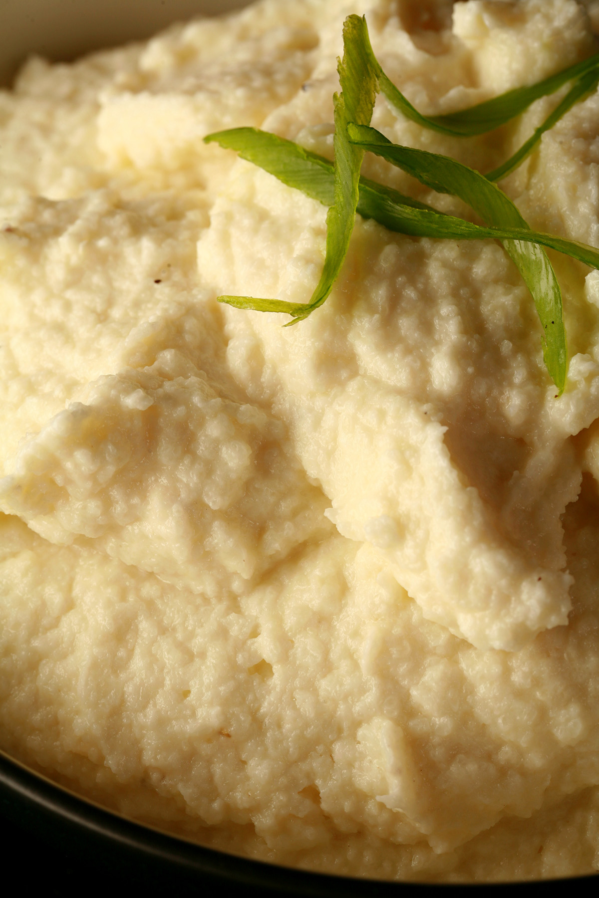 A close up view of a bowl of low carb cauliflower mash, with sliced green onions on top.