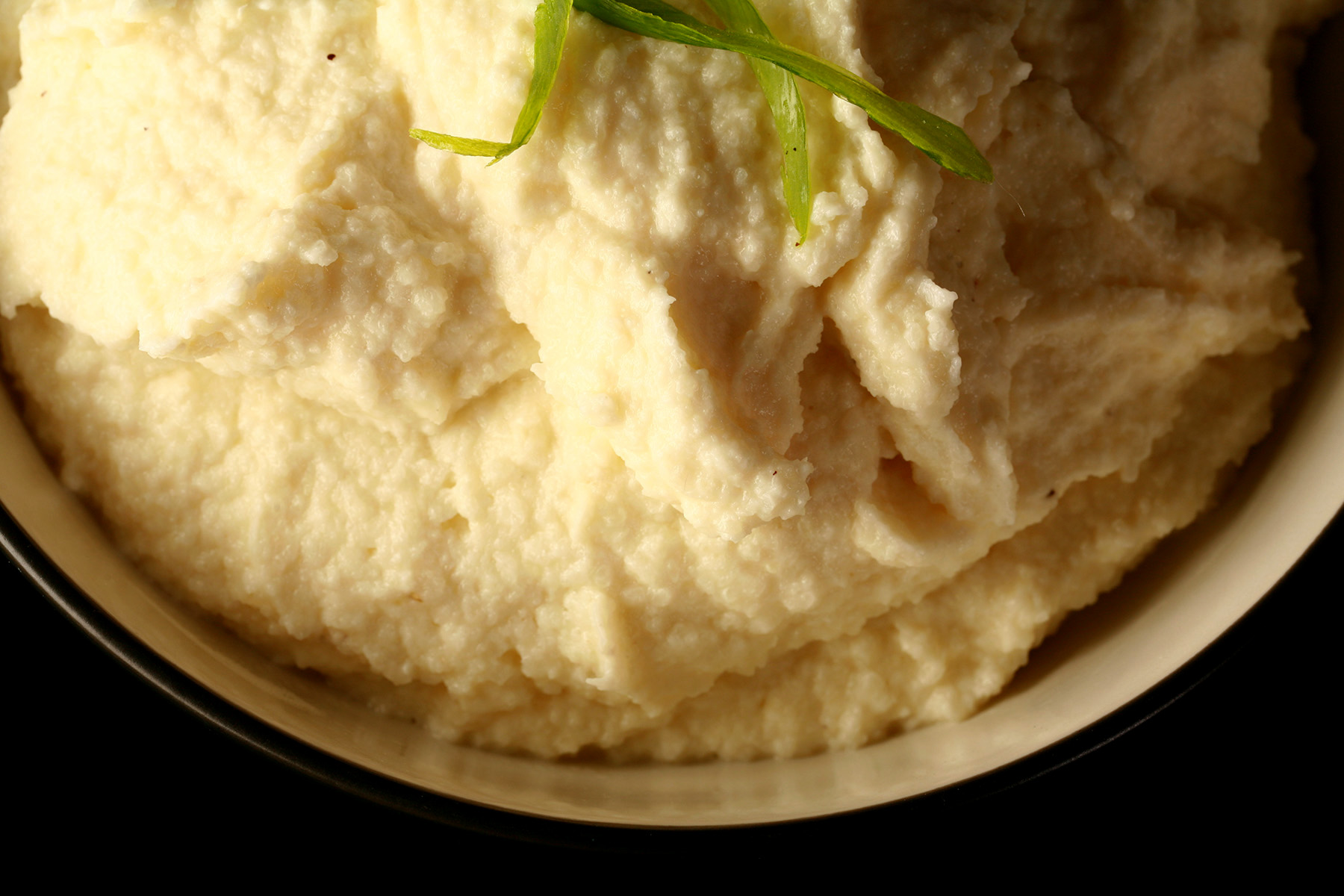 A close up view of a bowl of mashed cauliflower, with sliced green onions on top.