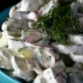A blue bowl of low carb creamy cumber salad, garnished with a sprig of fresh dill.