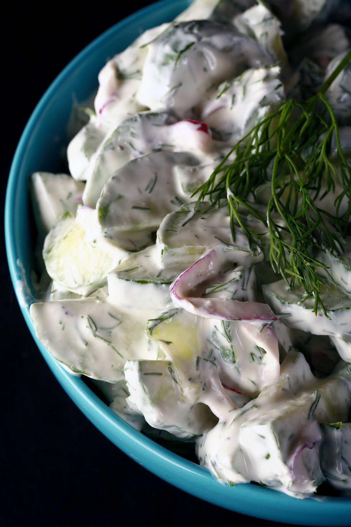 A blue bowl of low carb creamy cumber salad, garnished with a sprig of fresh dill.