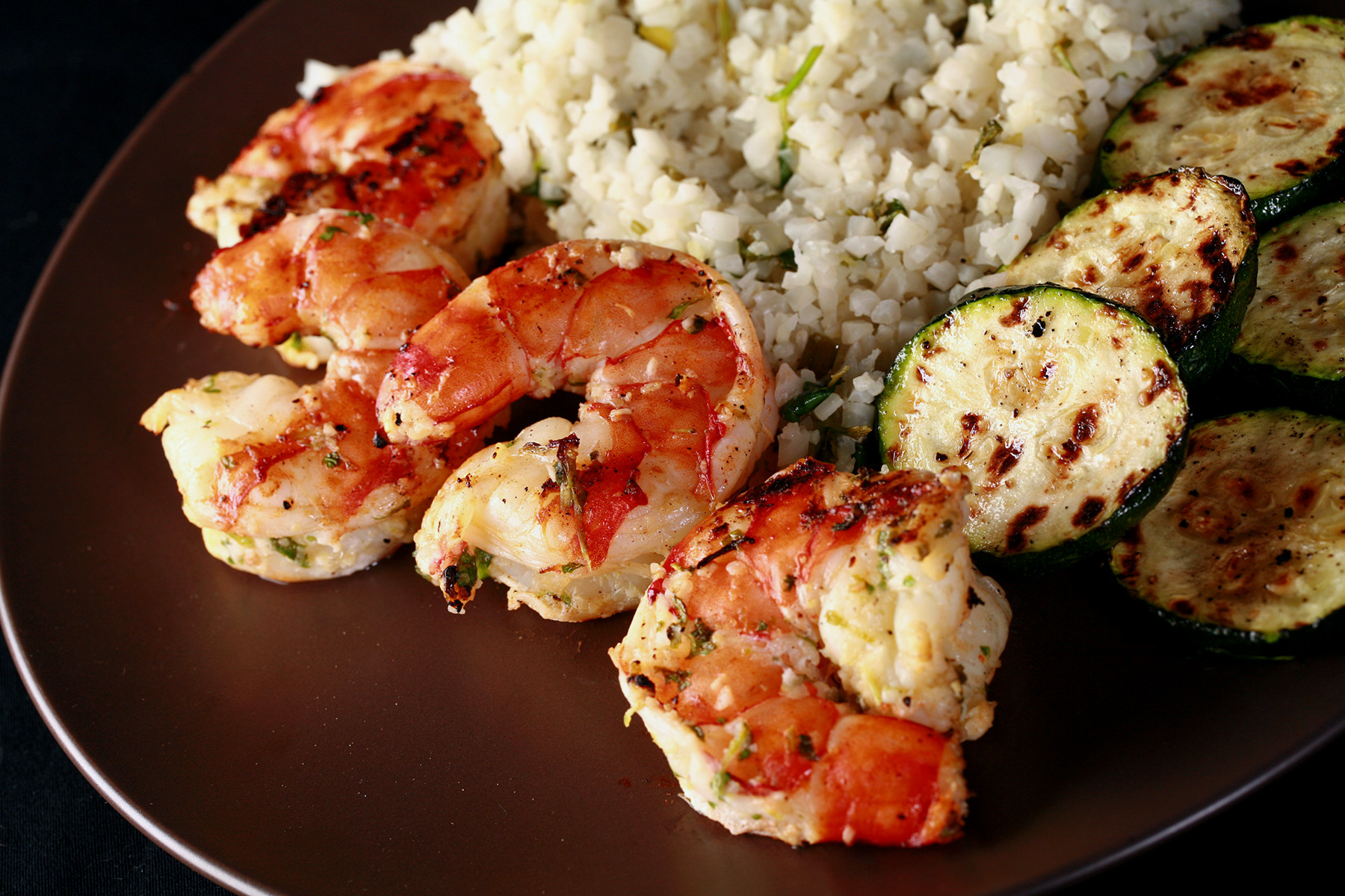 Jumbo grilled cilantro lime shrimp on a plate with keto cauliflower rice and grilled zucchini.