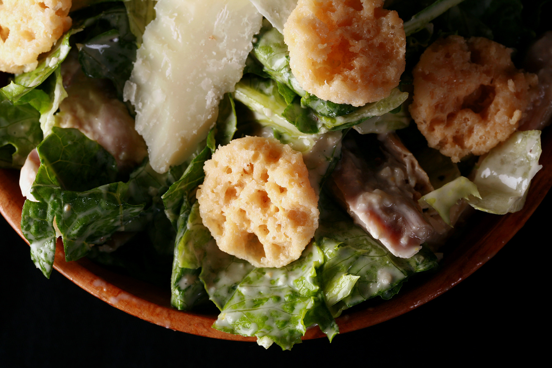 A bowl of keto Caesar salad with parmesan shreds and croutons on top.