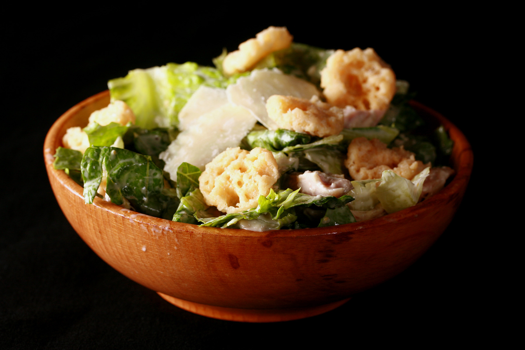 A bowl of low carb Caesar salad with parmesan shreds and croutons on top.