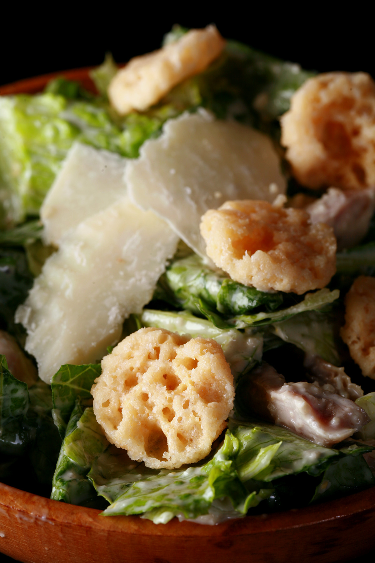 A bowl of keto Caesar salad with parmesan shreds and croutons on top.