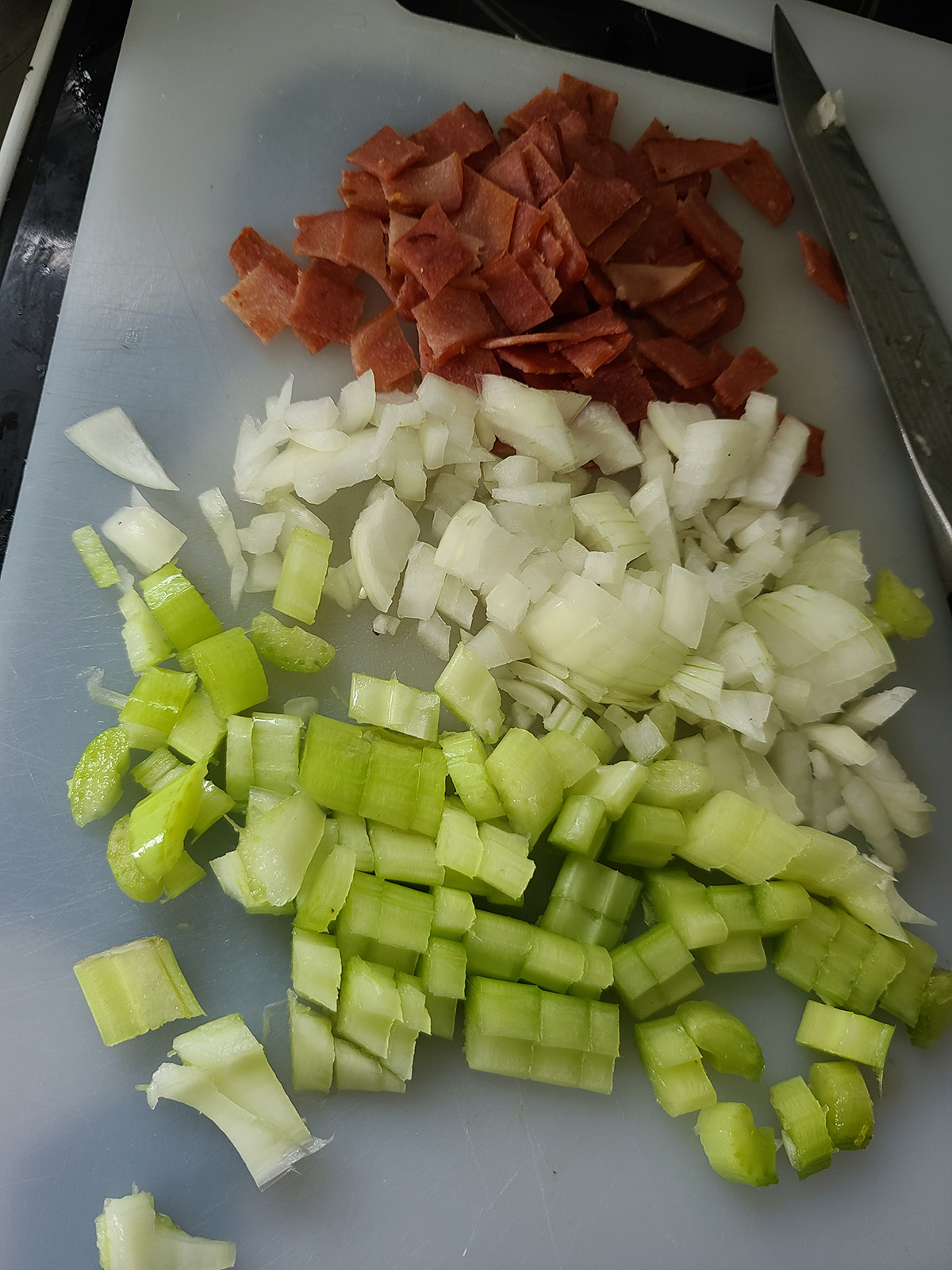 Chicken bacon, onion, and celery chopped on a white cutting board.