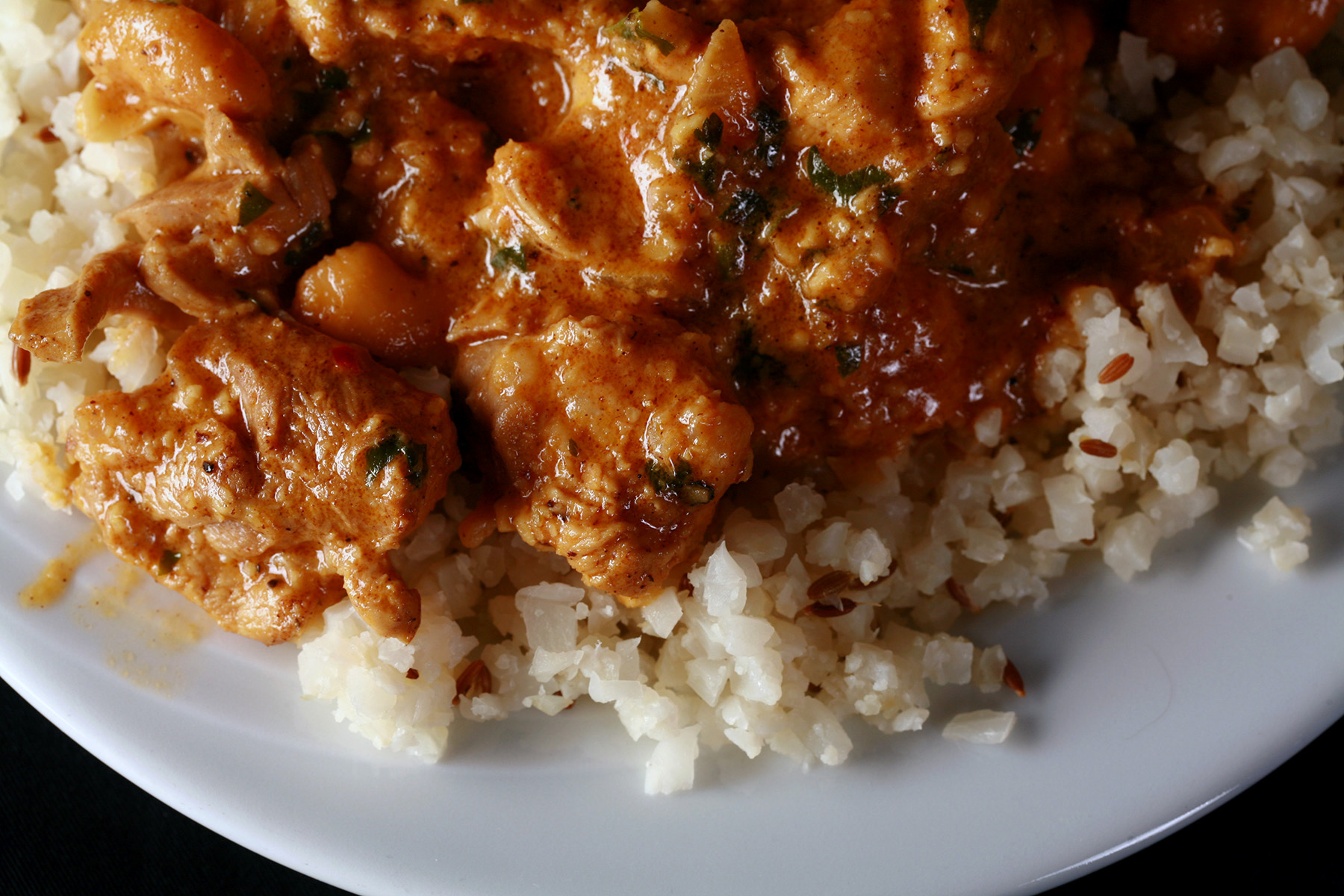 A plate of low carb chicken korma, served on a bed of jeera rice made from cauliflower.