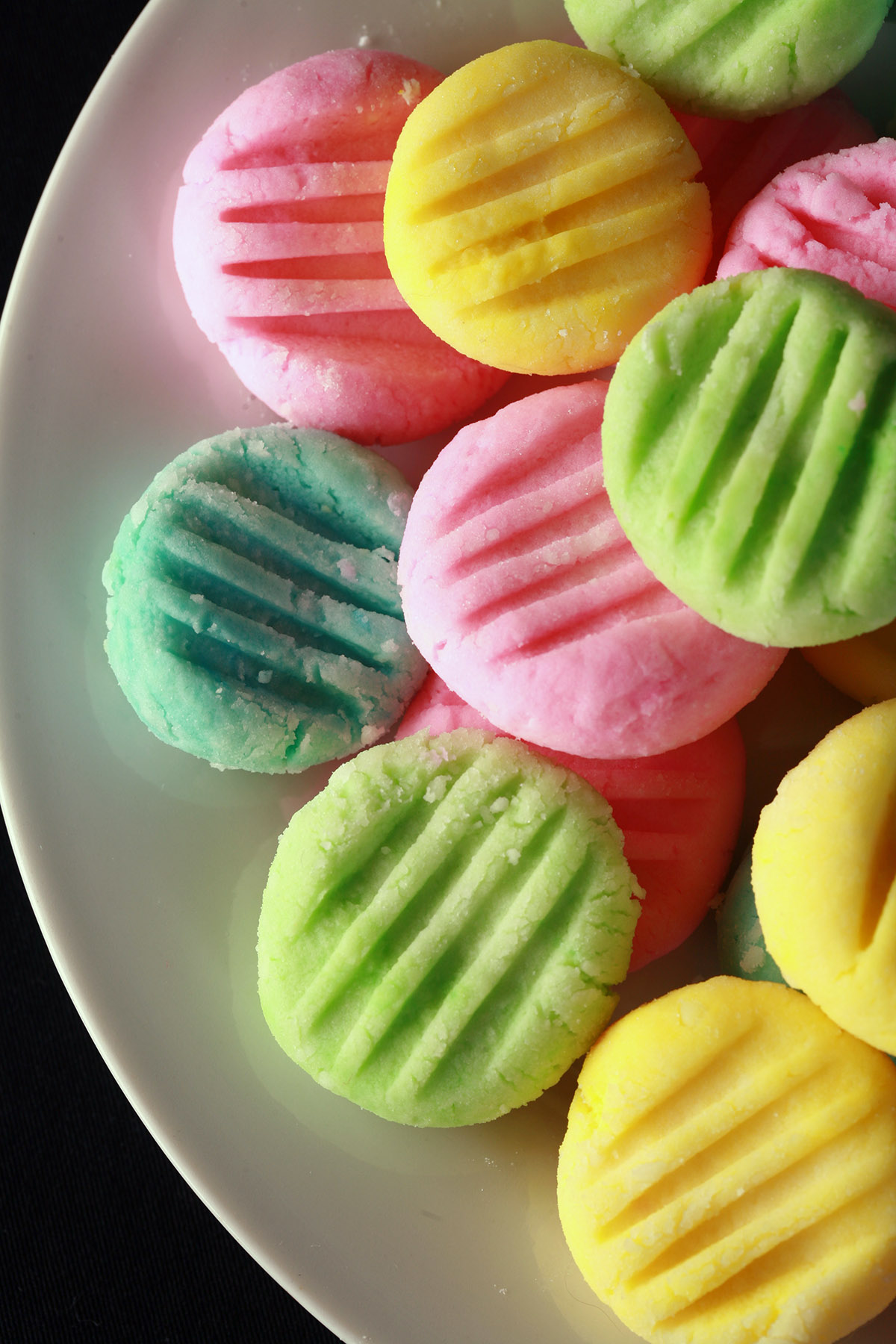 A plate piled high with low carb cream cheese mints. They are pink, yellow, green, and blue.