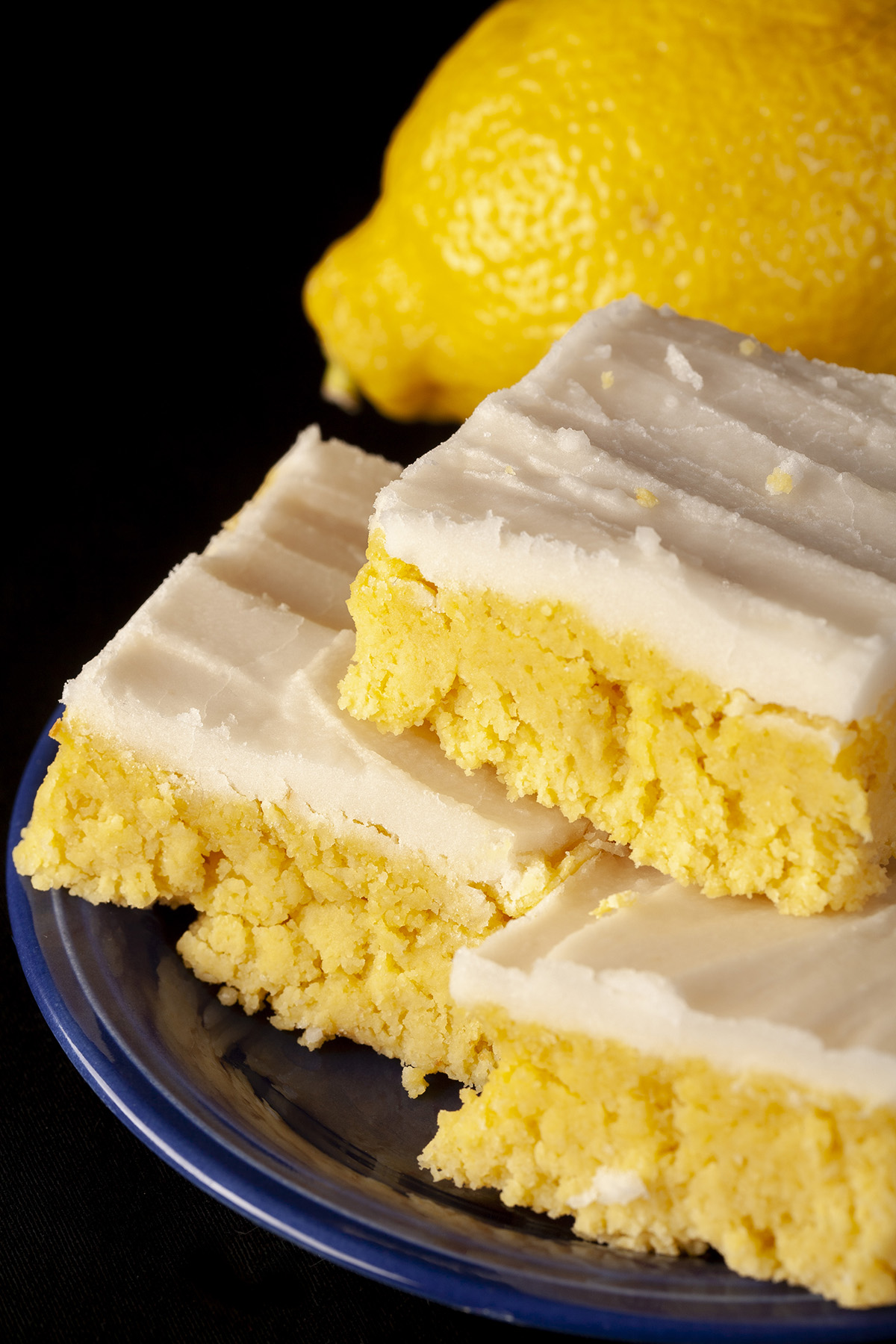 A plate of low carb chewy lemon bars, each topped with white sugar free frosting.