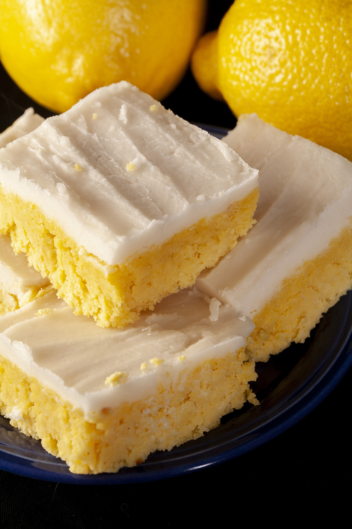 A plate of keto chewy lemon bars, each topped with white sugar free frosting.