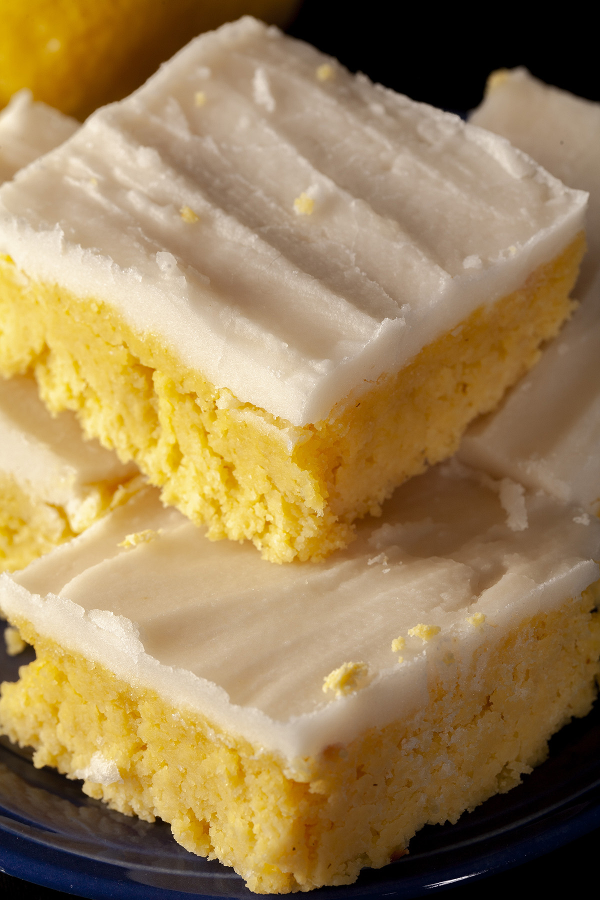 A plate of keto chewy lemon bars, each topped with white sugar free frosting.