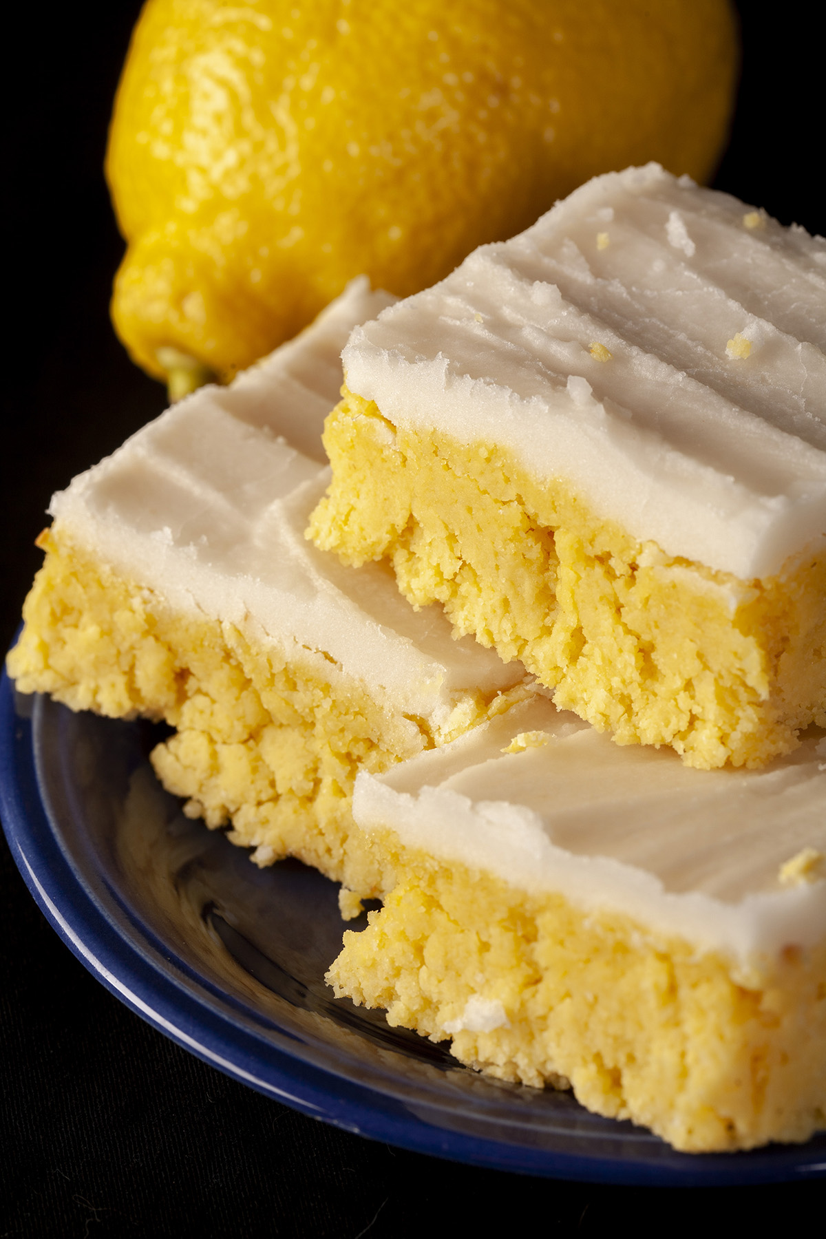 A plate of low carb chewy lemon bars, each topped with white sugar free frosting.