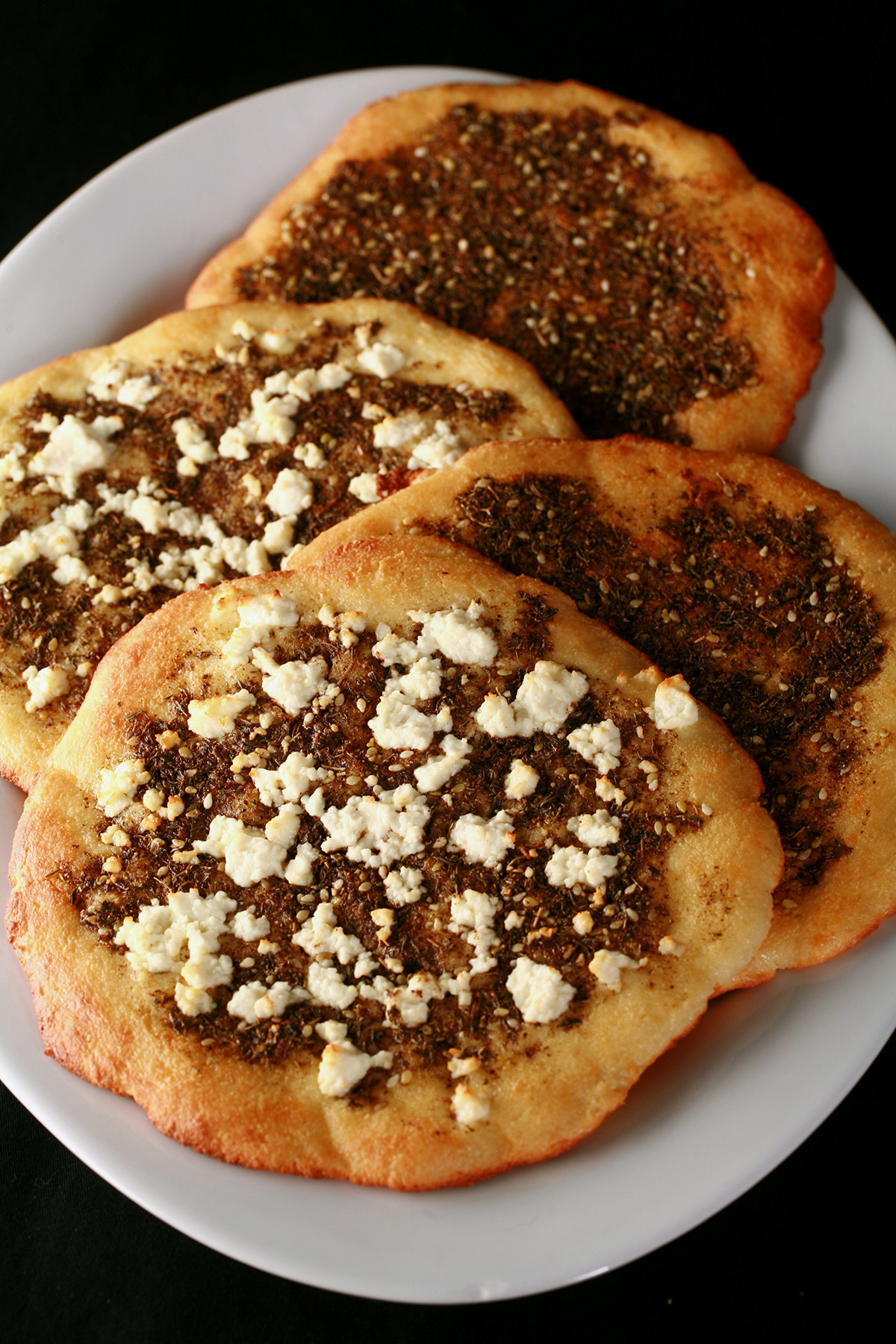 A white platter with 4 keto manakish on it. 2 are topped with Zaatar, 2 with Za'atar and cheese.