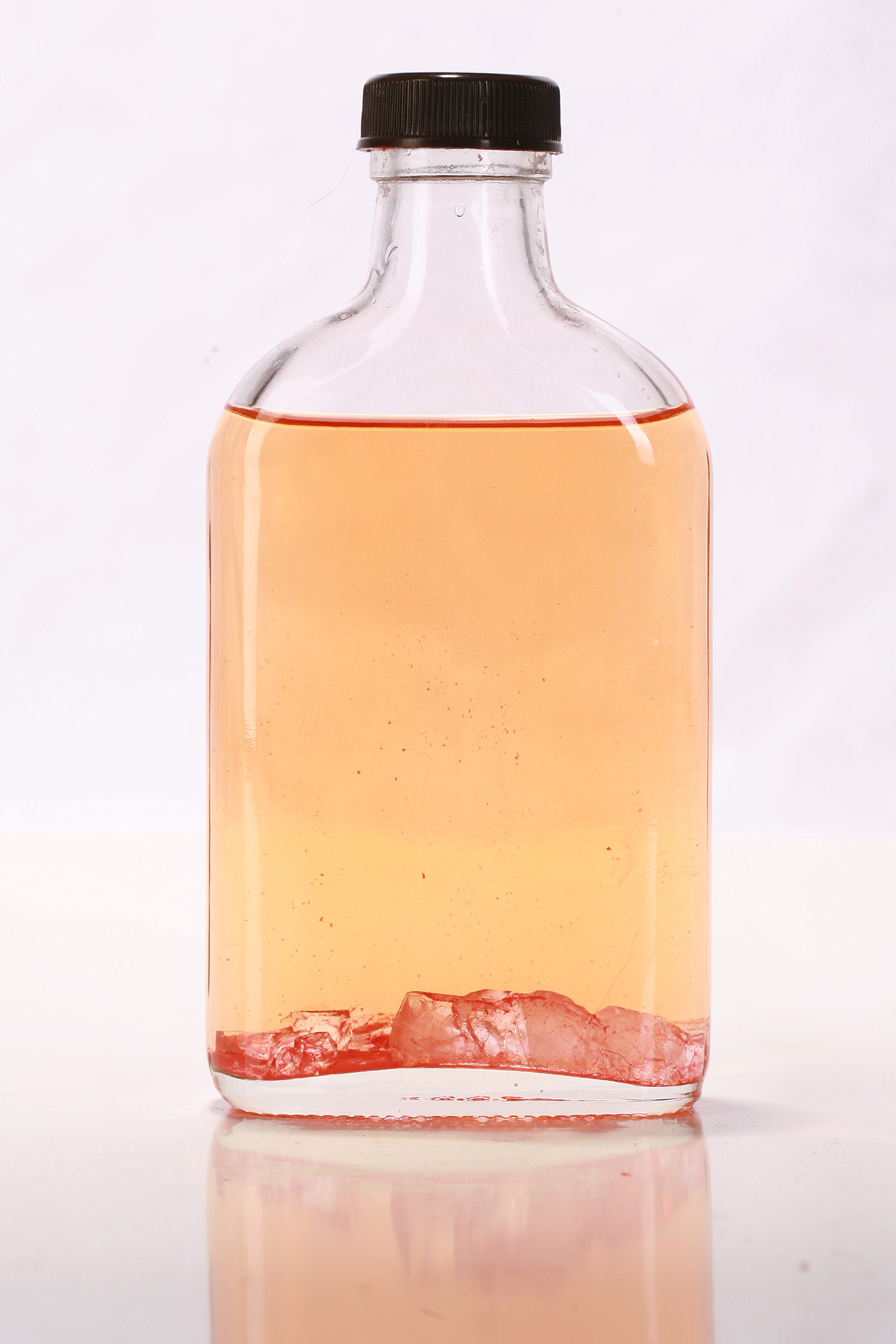 A small glass flask of watermelon homemade sour puss liqueur, with a layer of crystals in the bottom of the bottle.