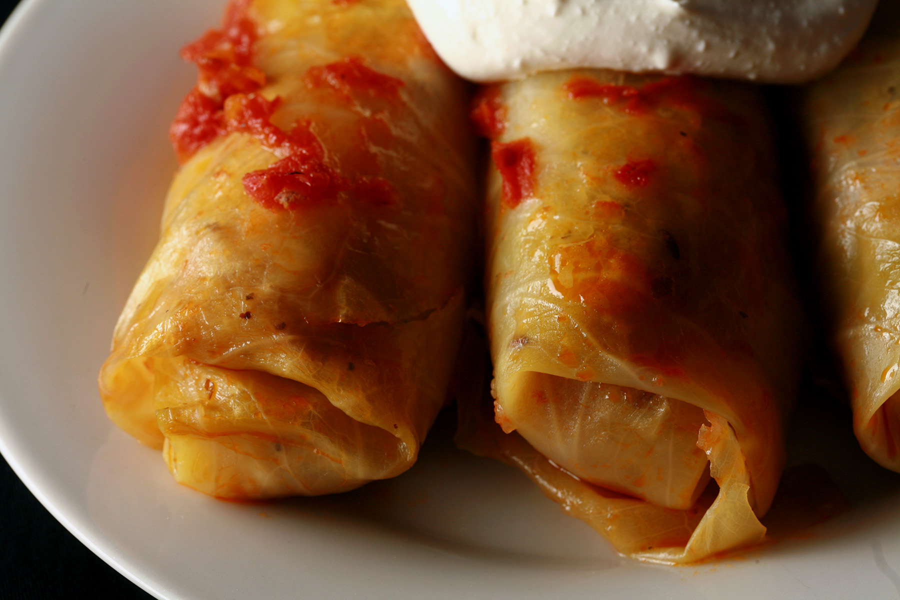 Keto cabbage rolls on a plate, garnished with a large dollop of sour cream.