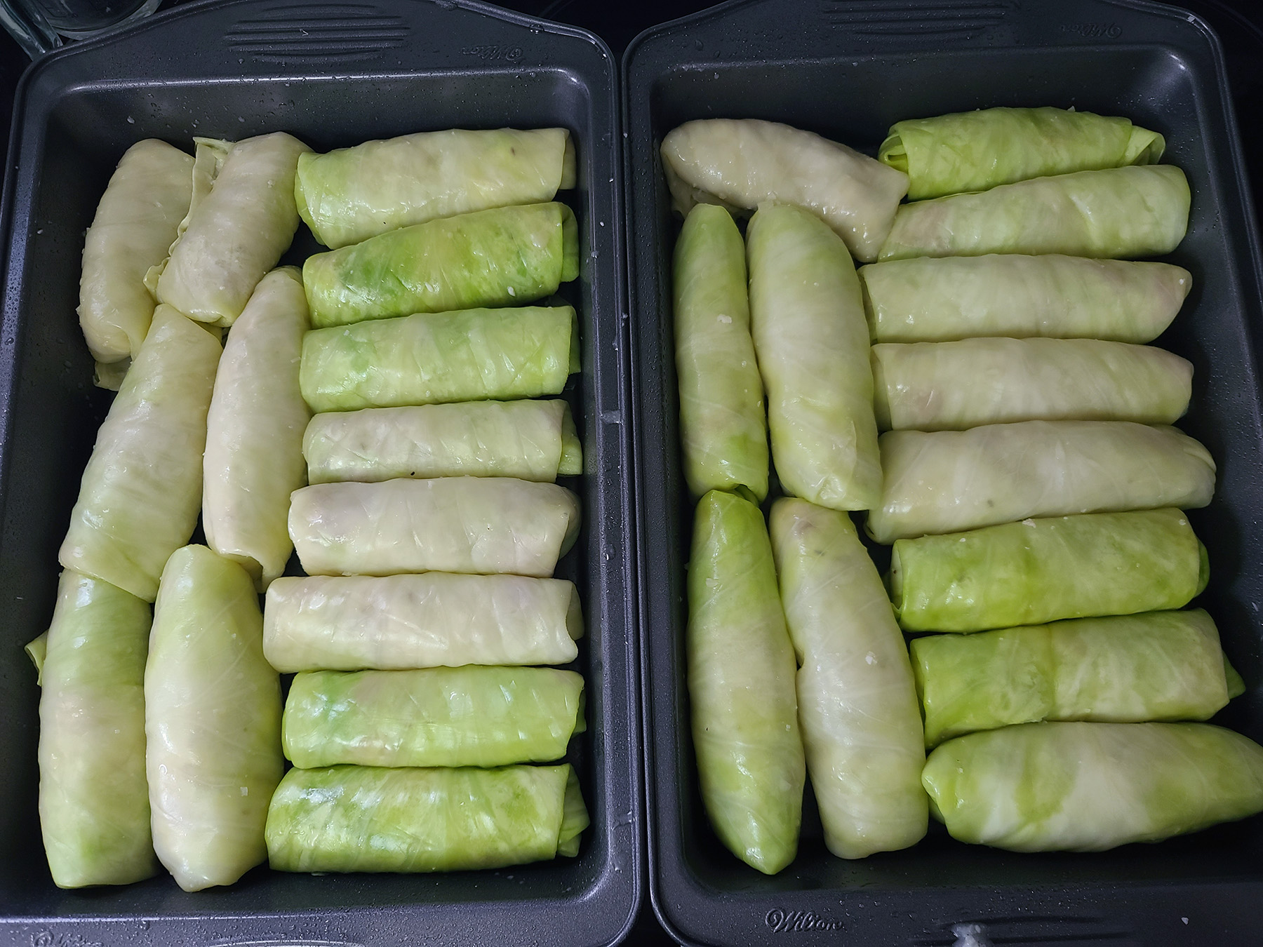 Two baking pans full of uncooked cabbage rolls.