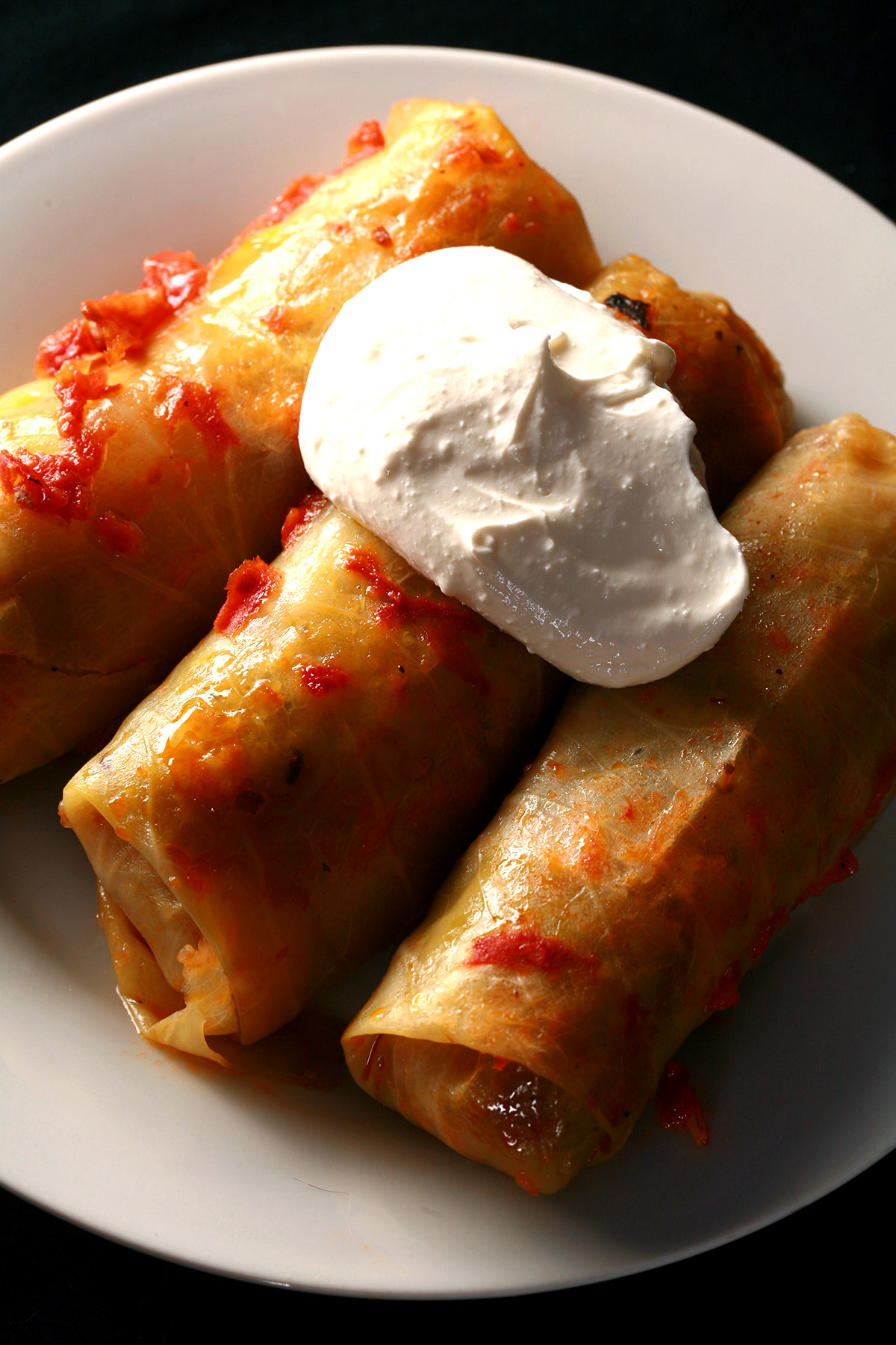 Keto cabbage rolls on a plate, garnished with a large dollop of sour cream.