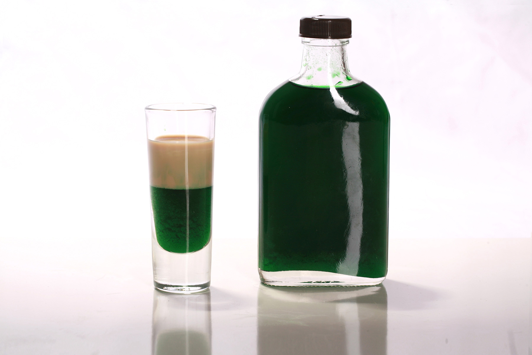 A layered shot glass of sugar-free creme de menthe and keto Irish cream next to a small bottle of low carb creme de menthe.