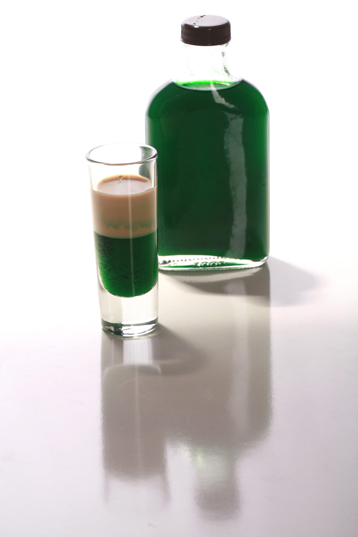 A layered shot glass of sugar-free creme de menthe and keto Irish cream in front of a small bottle of low carb creme de menthe.
