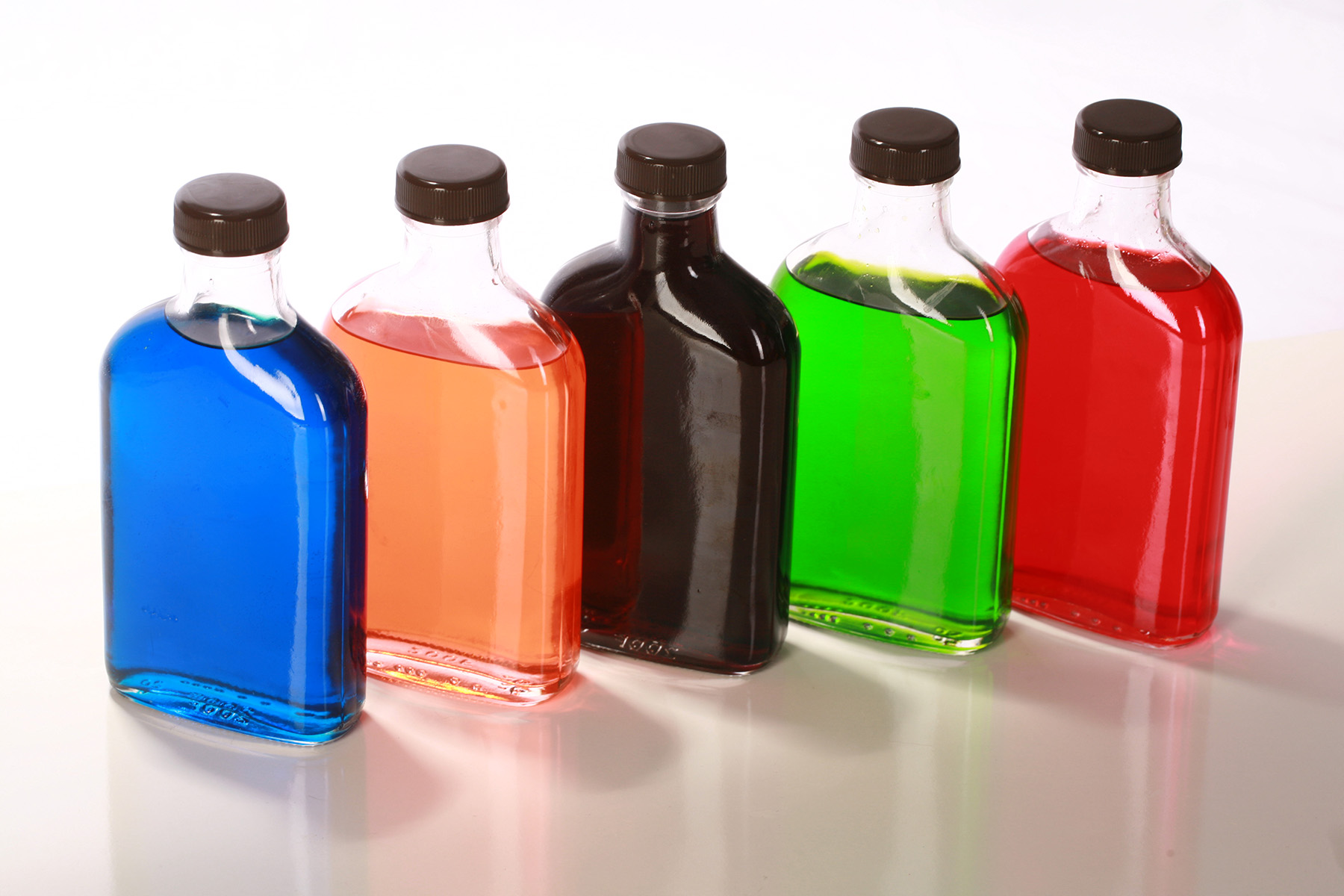 A line of 5 small bottles of brightly coloured homemade sugar-free sour puss liqueur. Blue, Pink, Green, Red, and purple.