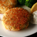 Two keto fish cakes on a plate with low carb tartar sauce and steamed broccoli.