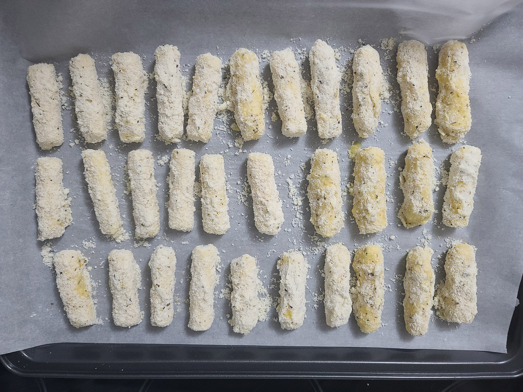 An overhead view of the prepared keto mozzarella sticks on a baking sheet.