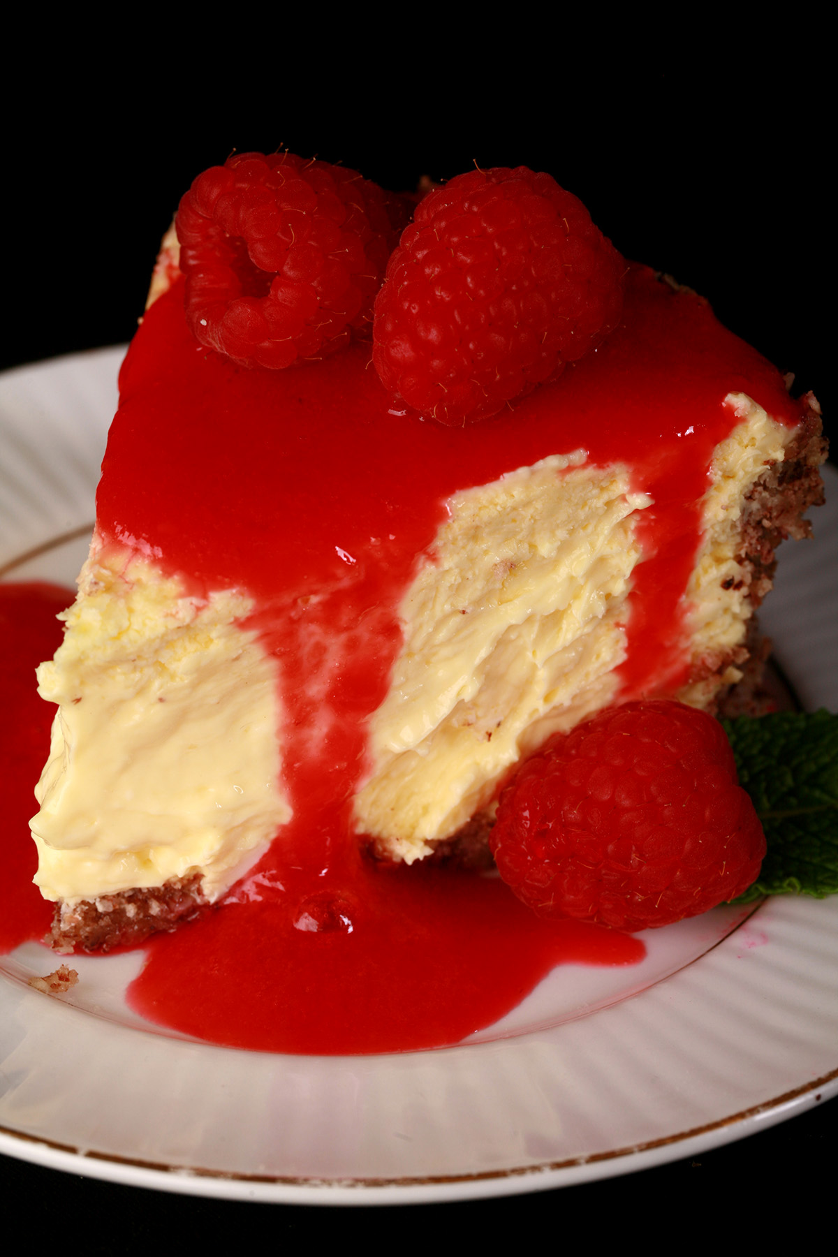 A slice of vanilla keto cheesecake on a plate, drizzled with sugar free raspberry sauce.