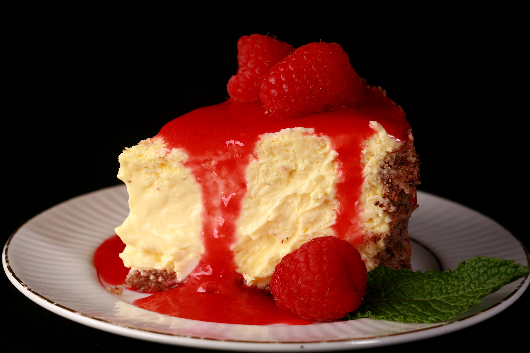 A slice of vanilla sugar free cheesecake on a plate, drizzled with sugar free raspberry sauce.