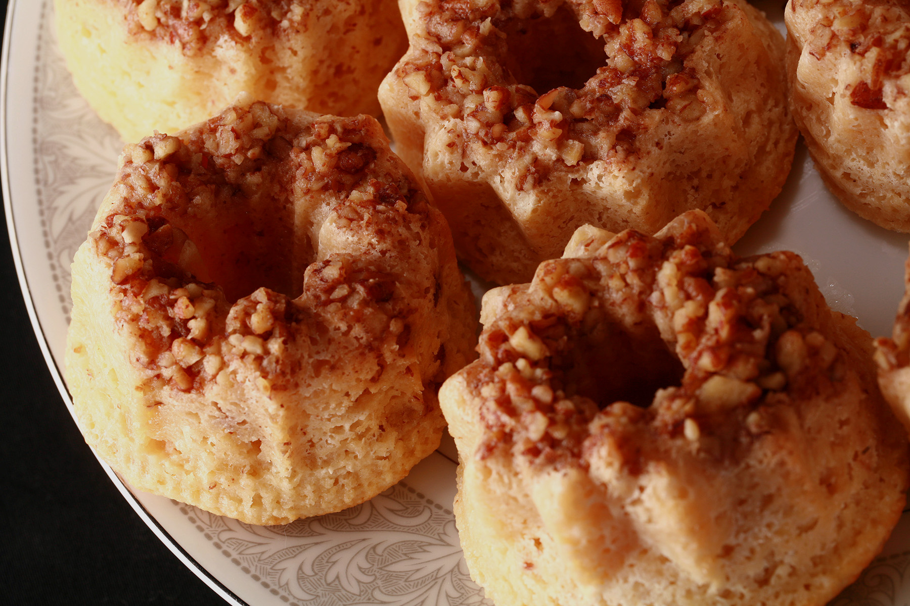 A plate of mini keto rum cake bundts, each with pecan topping.