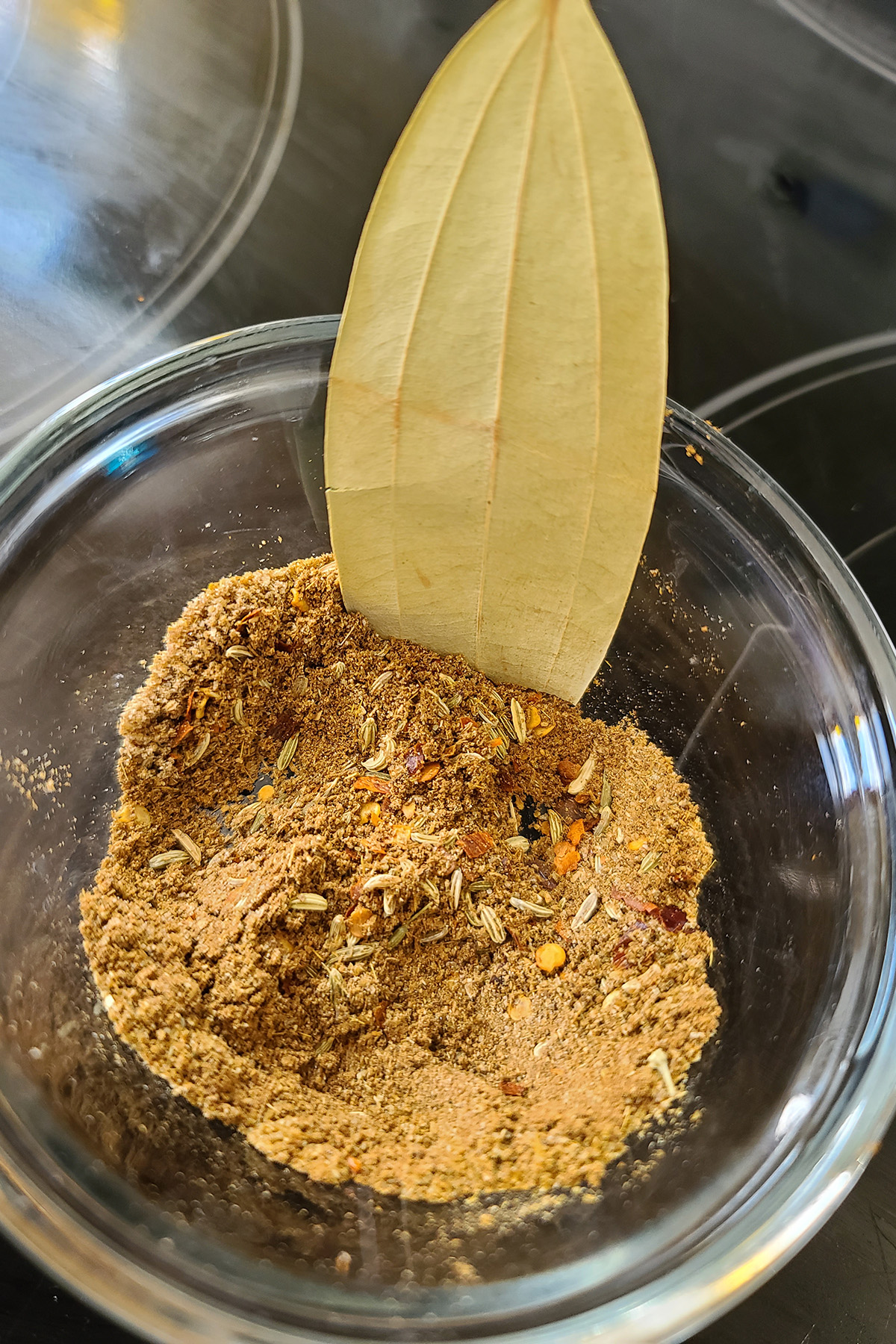 A small glass bowl of spices, with a bay leaf sticking out.