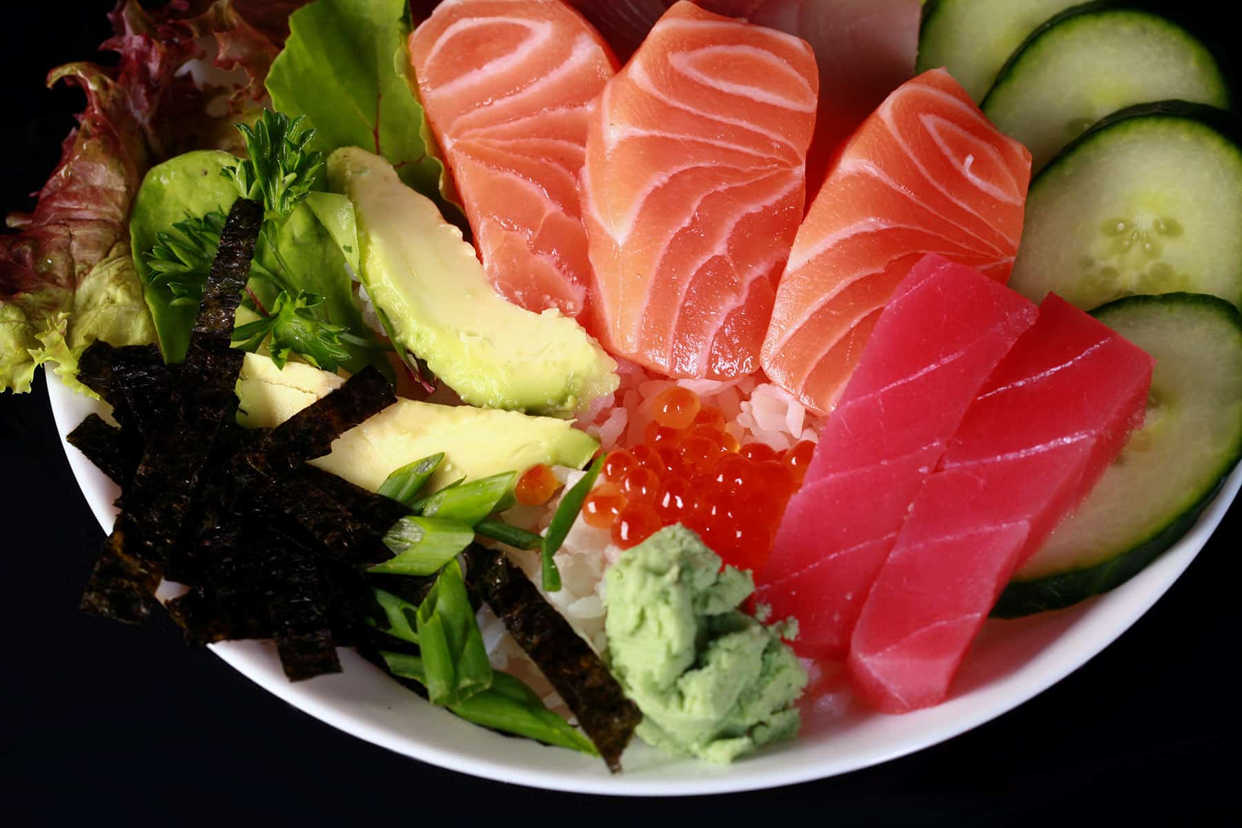 A close up view of chirashi - raw fish slices and vegetables arranged on a bowl of rice.