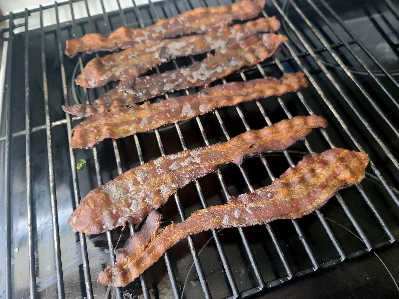 Bacon slices smoking in a large smoker.