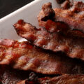 A plate piled high with crispy smoked bacon slices.