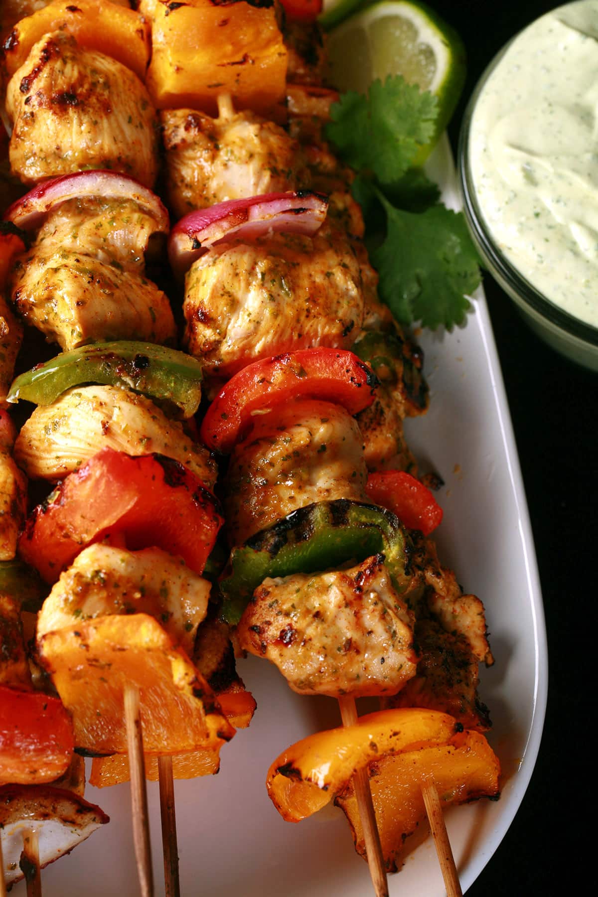 A tray of chicken fajita kebabs with a bowl of avocado crema next to it.