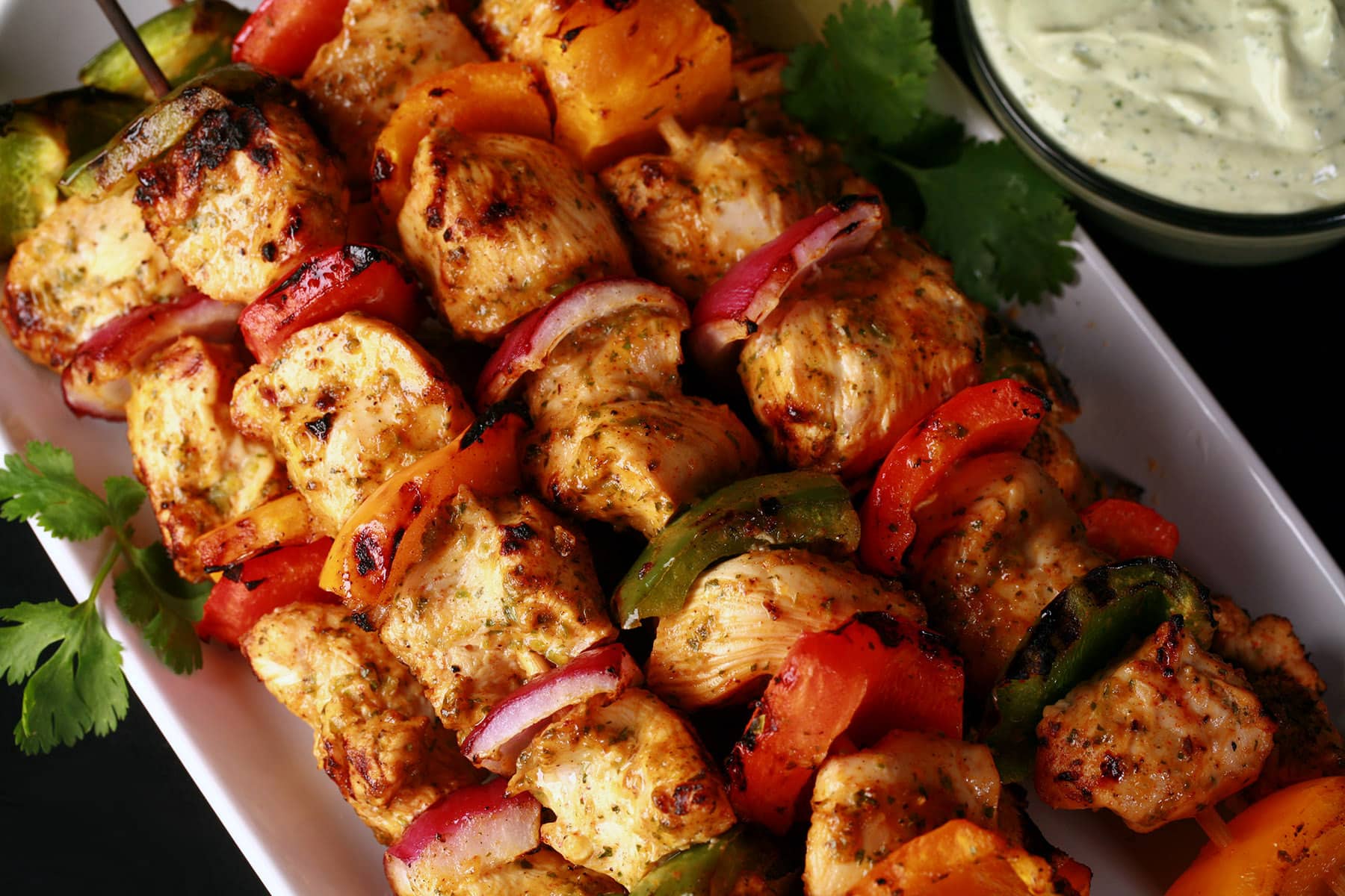 A tray of chicken fajita skewers with a bowl of avocado crema next to it.