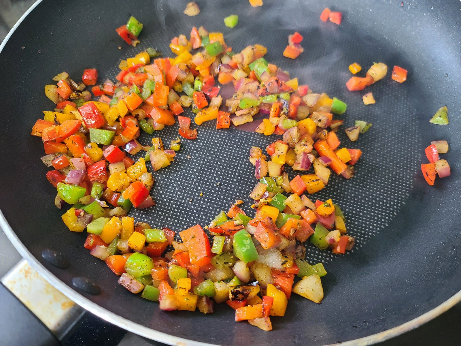 Chopped up bell peppers cooking in a nonstick pan.