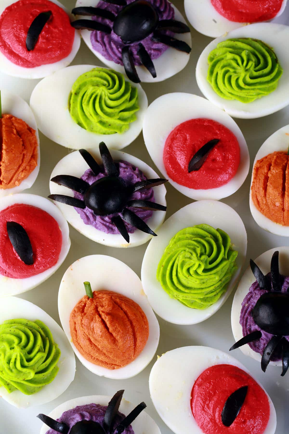 A plate of Halloween deviled eggs, with a variety of fillings and styles in red, orange, lime green, and purple.