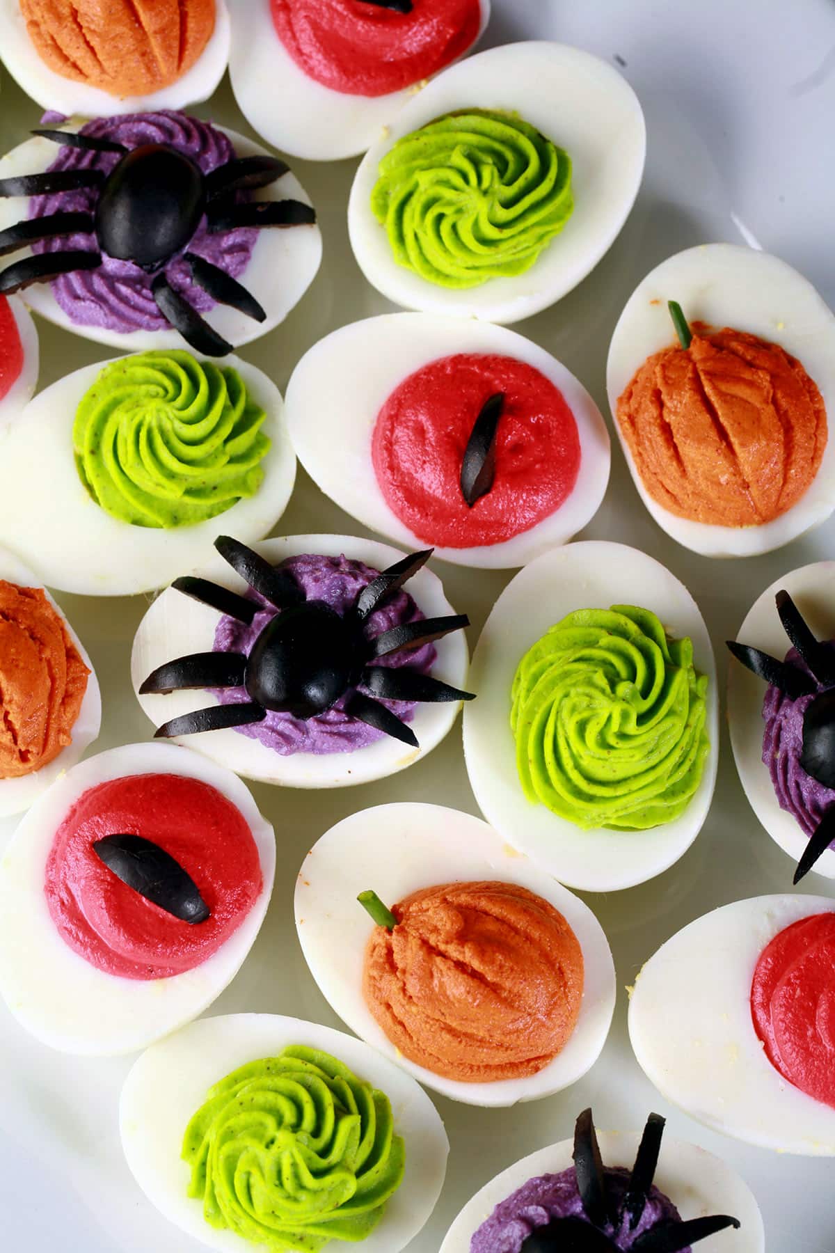 A plate of Halloween deviled eggs, with a variety of fillings and styles in red, orange, lime green, and purple.