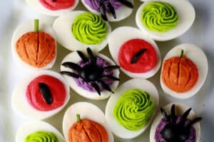 A plate of Halloween deviled eggs, with a variety of fillings and styles in red, orange, lime green, and purple.